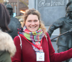 A smiling woman on a city trip to Amsterdam. She is standing in front of a Rembrandt statue.