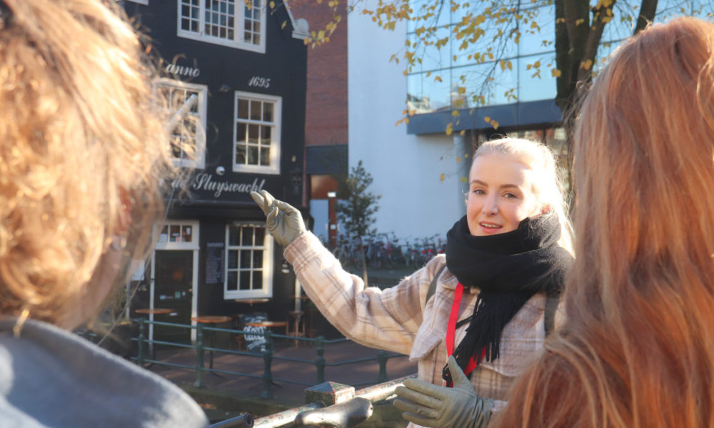 Amsterdamliebe Tourguide zeigt auf das Rembrandthuis vor dem Café Sluyswacht