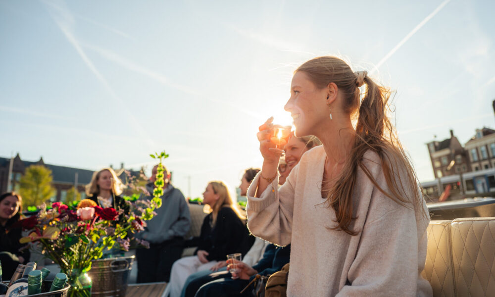 Woman with a drink on a boat tour. Enjoying a city trip to Amsterdam.