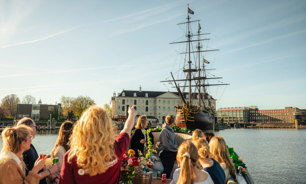 People on a boat tour in Amsterdam. A tall ship is visible in the background.