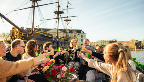 Friends enjoying a boat trip in Amsterdam, cheering with drinks. Group of people on a boat having fun.