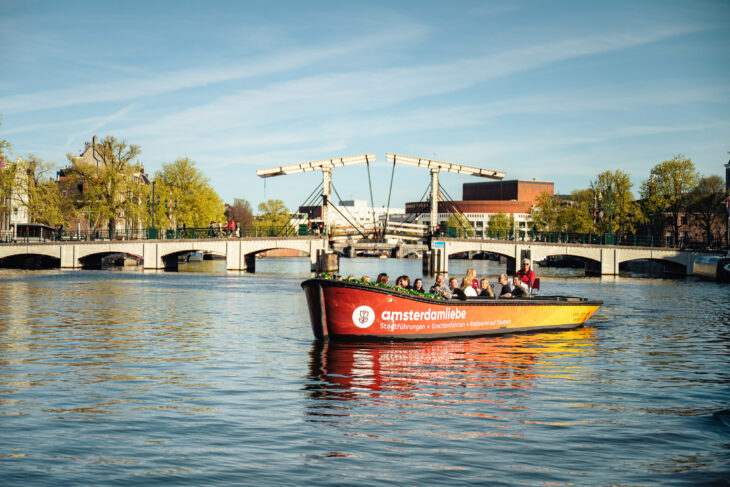A red and yellow canal boat on a sunny day. People on a guided tour.