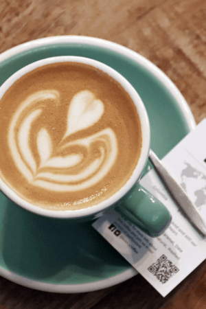A black and white photo of a coffee cup with a leaf design on a saucer. The coffee cup and saucer are placed on a table.