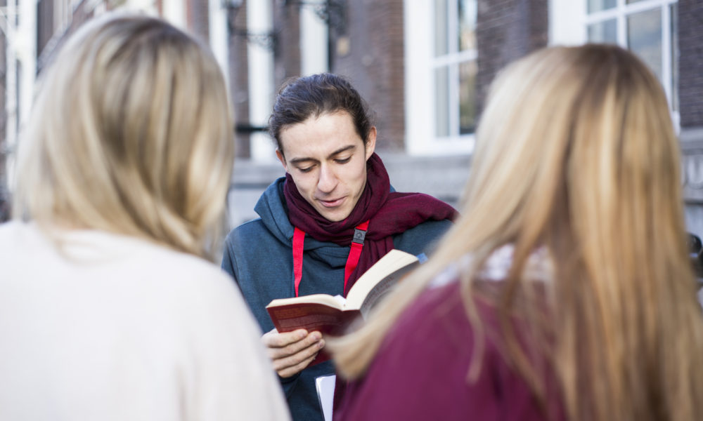Three students talking and reading a book. Young people in Amsterdam.