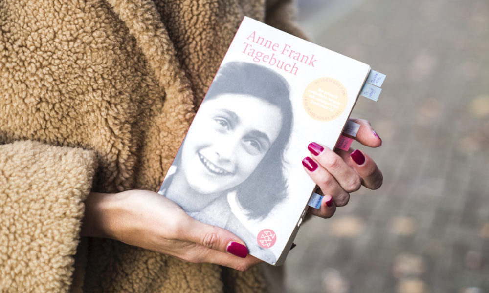 A person holding a book about Anne Frank. The book cover features a photo of Anne Frank.