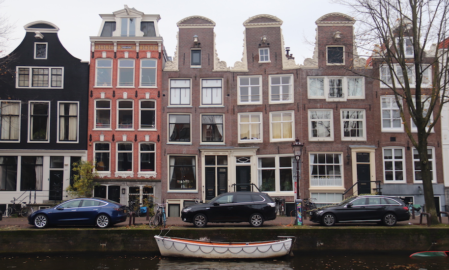 Autos parken vor schiefen Grachtenhäusern an der Gracht