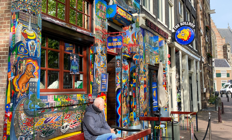 Mann sitzt vor dem bunt bemalten Eingang von the Bulldog Coffeeshop, an dem die Amsterdamliebe-Rotlichttour auch vorbei kommt.