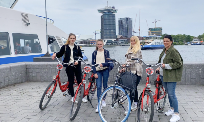 Amsterdamliebe Tourguide Julia steht mit Tourteilnehmern am Hauptbahnhof neben einer Fähre mit Blick auf dem A'dam Tower