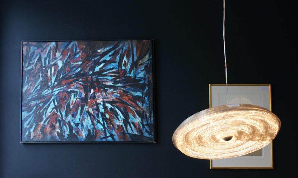 Modernes, buntes Kunstwerk und moderne Lampe vor dunkelblauer Wand