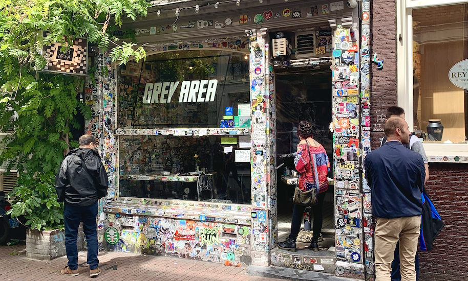Menschen warten vor dem mit Stickern beklebten Grey Area Coffeeshop.