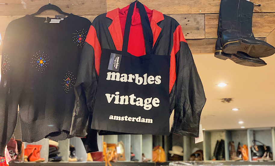 Schwarze Marbels Vintage Amsterdam Stofftasche hängt neben Pullover und Stiefel