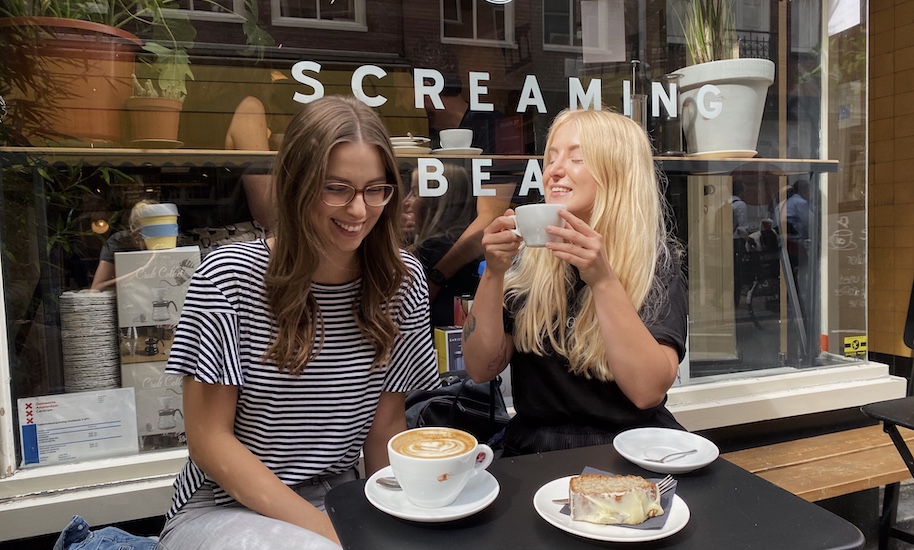 Zwei lachende Frauen sitzen vor dem Streaming Beans Café mit einem Kaffee