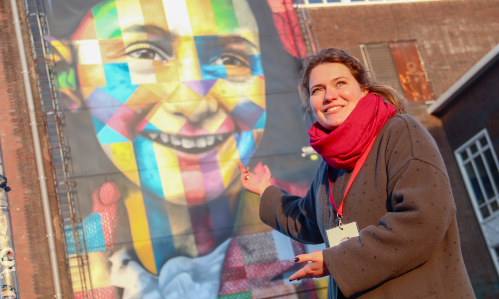 A woman standing next to a colorful mural. The mural features a smiling face.