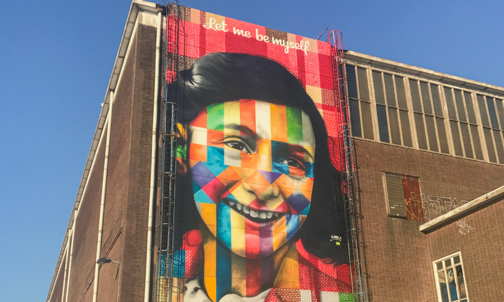 A large colourful mural of a smiling woman's face. The mural is on the side of a brick building.
