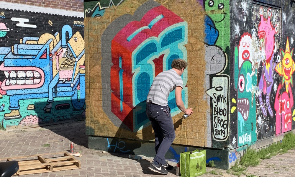 A man painting a vibrant mural on a brick wall in Amsterdam. The artwork features a mix of colours and shapes.