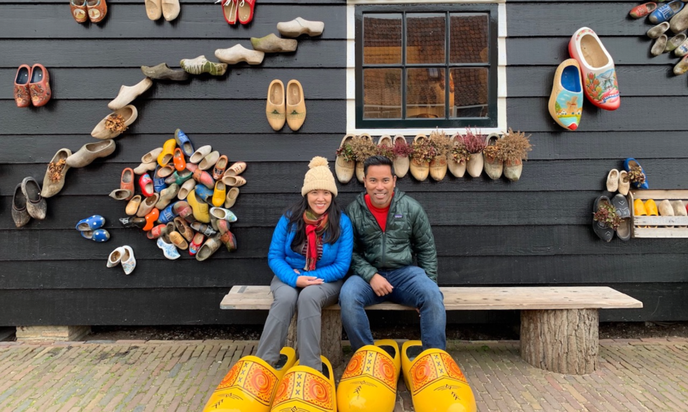 Couple sitting on bench with wooden shoes. Traditional Dutch footwear on display.