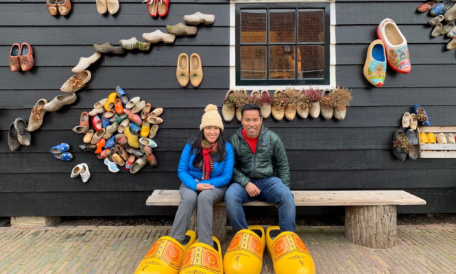 Amsterdamliebe Tourteilnehmer sitzen vor einer Holzschuhmanufaktur und haben übergroße Holzschuhe an