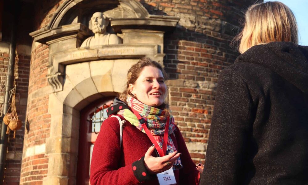 Two women standing outside a brick building. One woman is wearing a red coat and a colorful scarf.