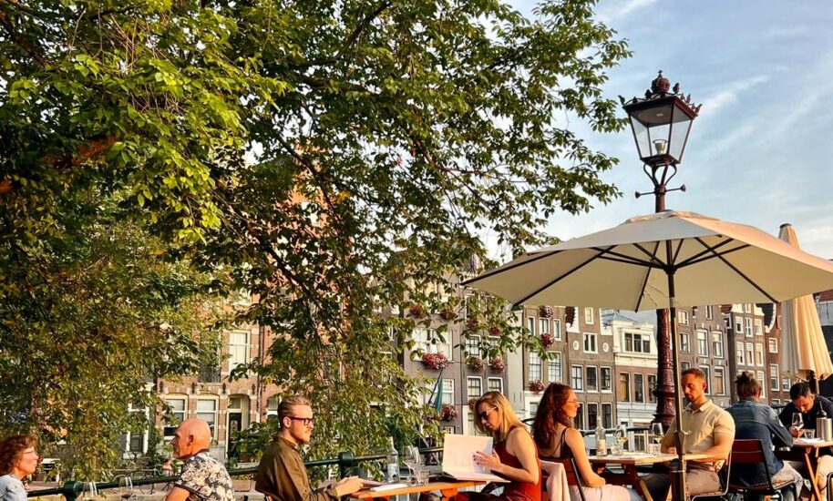 People enjoying a sunny day at an outdoor cafe. Tables and chairs set up on a brick sidewalk.