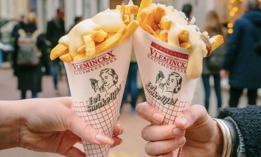 Two hands holding cones of French fries on a city street. Delicious Amsterdam street food.