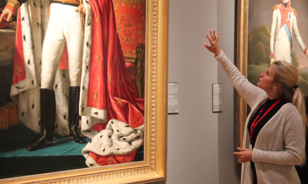 A woman looking at paintings. The paintings are of men in historical clothing.
