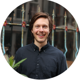 A smiling man in a black shirt standing in Amsterdam.
