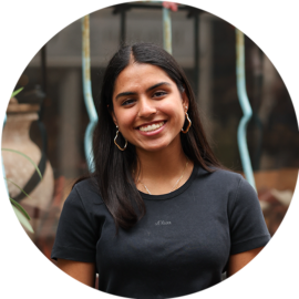 A young woman with long dark hair and gold hoop earrings. She is smiling and wearing a black t-shirt.