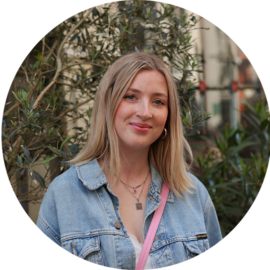 A young woman with blonde hair smiling. She is wearing a denim jacket.