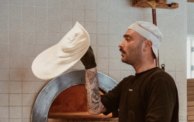 A chef preparing pizza dough. He is standing by a brick oven.