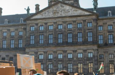 People protesting in front of a large building. They are holding signs and banners.