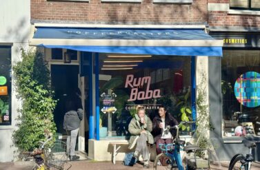 The Café Rumbaba in the Elandsgracht. A blue awning cafe with people sitting outside. A bike is parked in front.