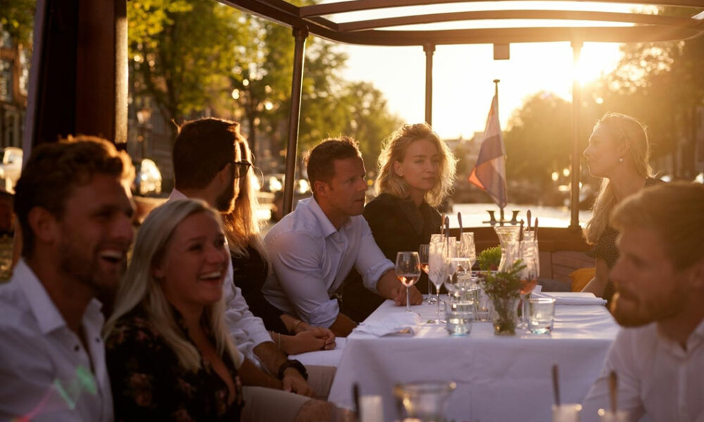 People enjoying a meal on a boat in Amsterdam. Glasses and plates on the table.
