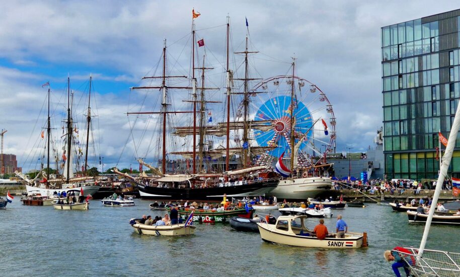 Sailing ships and boats in Amsterdam harbour. A large Ferris wheel is visible in the background.