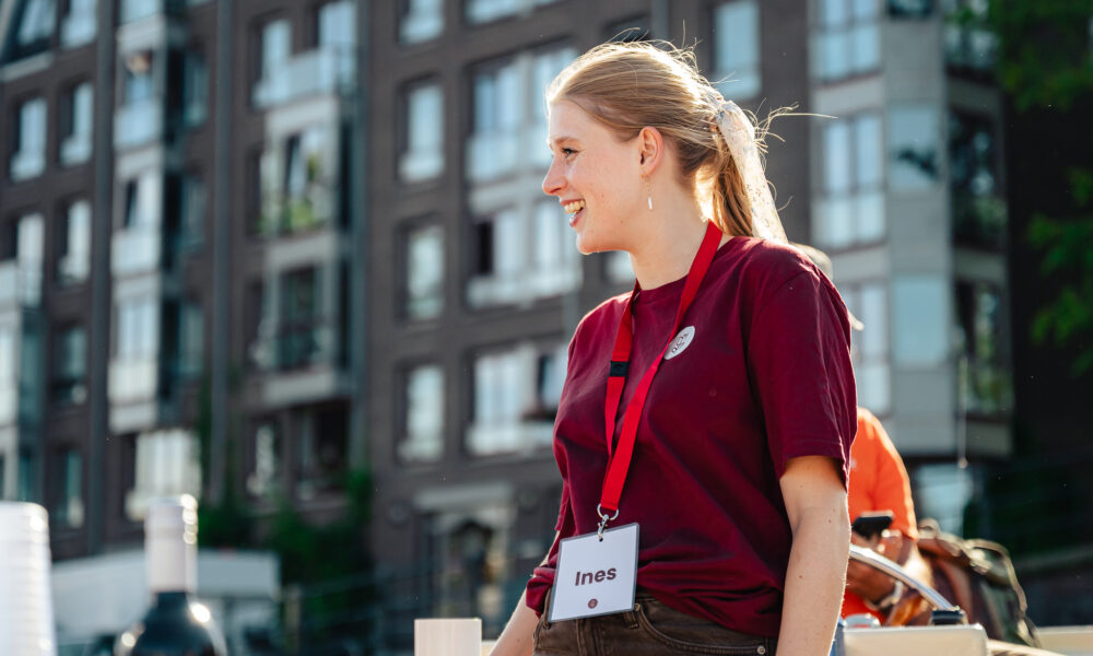A young woman wearing a red lanyard and a maroon t-shirt. She appears to be at an outdoor event.
