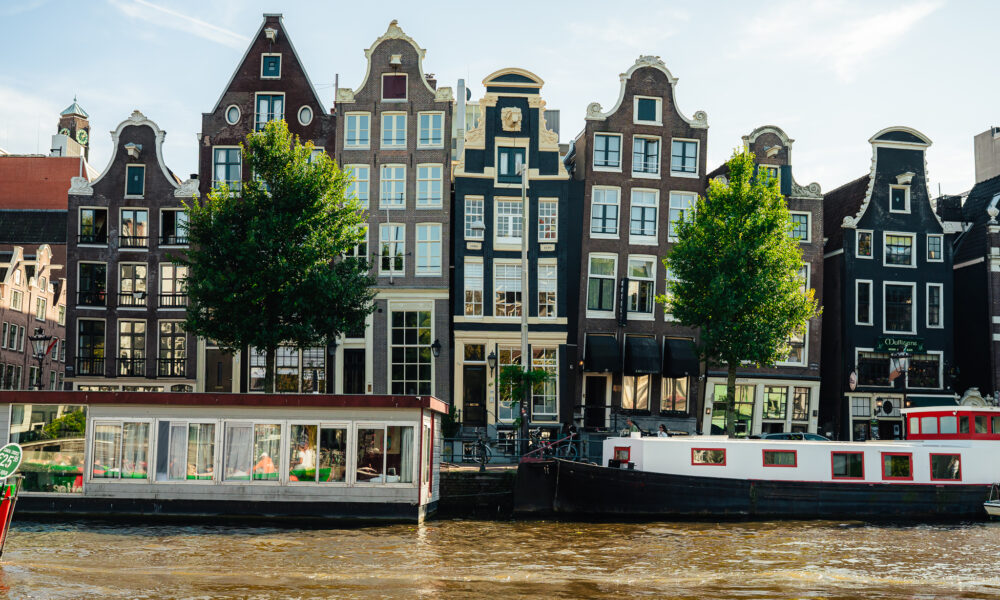 Traditional Amsterdam houses and boats on the canal. The houses are tall and narrow with ornate facades.