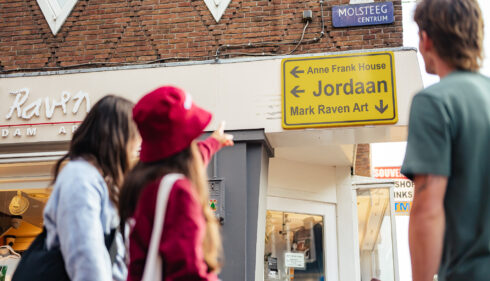 People walking on a street in Jordaan, Amsterdam. A yellow street sign with 'Jordaan' is visible.