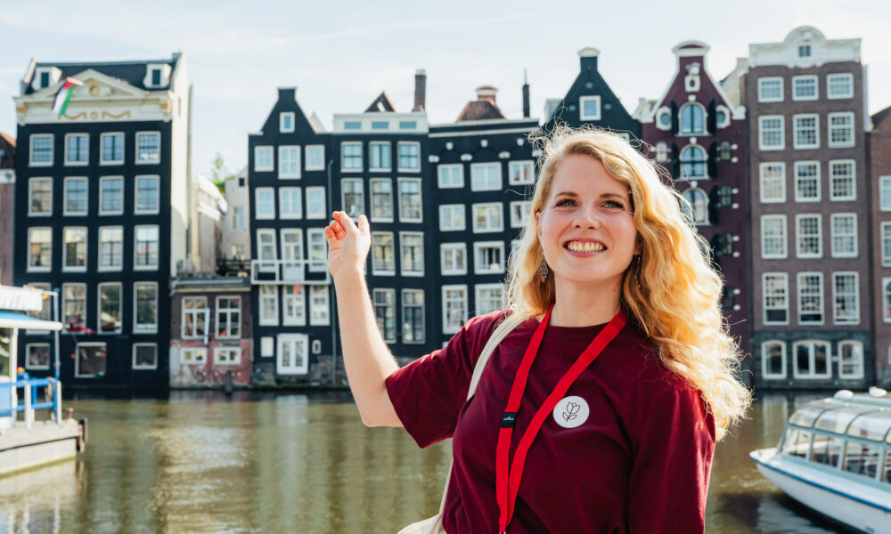Woman smiling on a city trip in Amsterdam. Colourful buildings in the background.