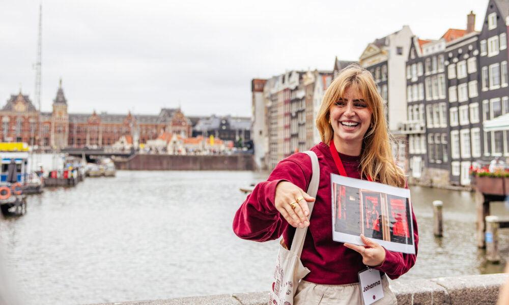 Smiling woman holding a travel guide. A picturesque canal in Amsterdam.