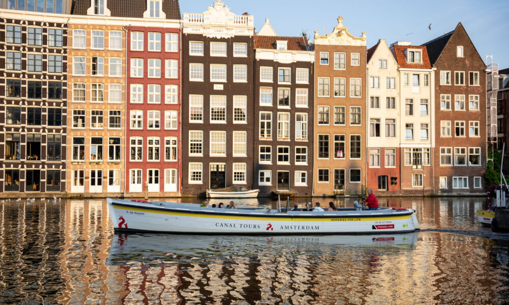 A boat on a canal in Amsterdam. Colourful buildings line the water.