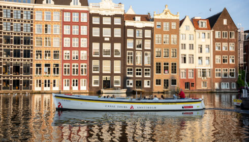 A boat on a canal in Amsterdam. Colourful buildings line the water.
