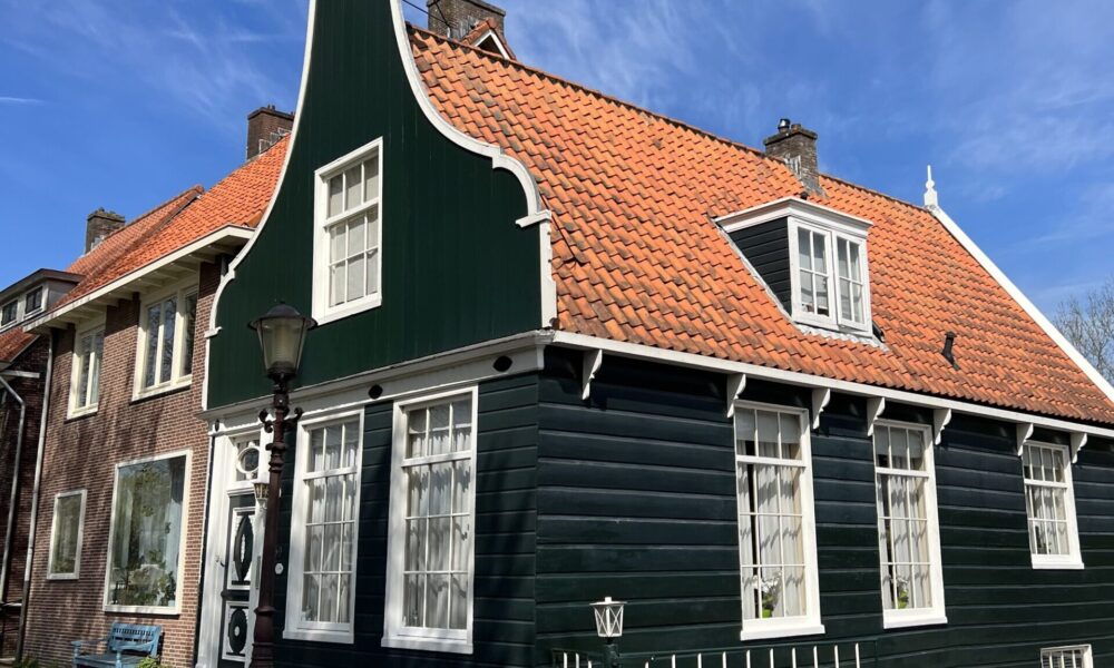 A traditional Dutch house with a green facade and red roof. The house features white trim and windows.