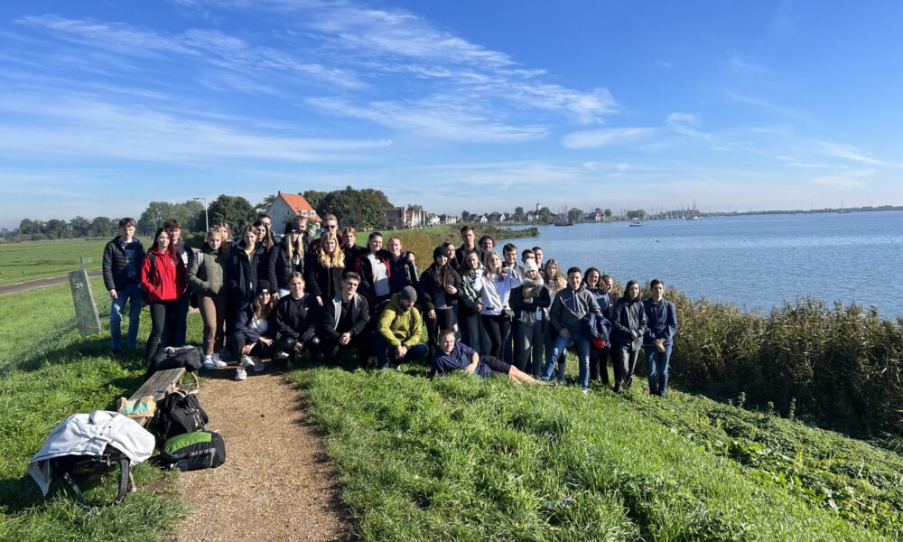 A group of people standing on a grassy hill. They are on a trip to Amsterdam.