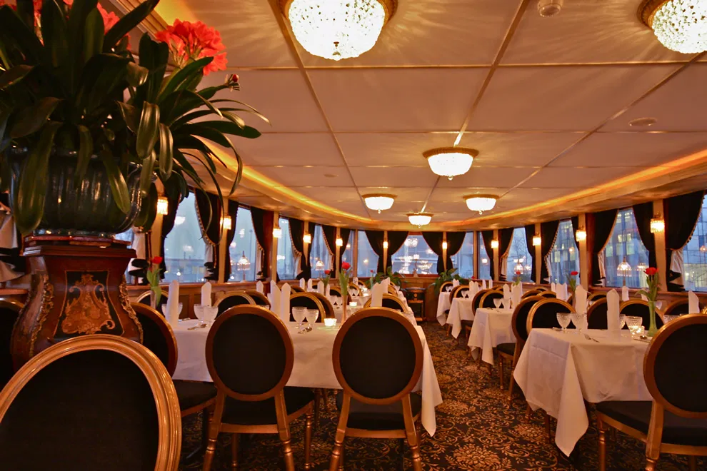 Luxurious dining area on a boat with white tablecloths and chairs. Elegant interior with large windows.