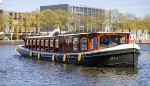 A houseboat on a canal in Amsterdam. The boat has a dark green hull and a wooden upper deck.