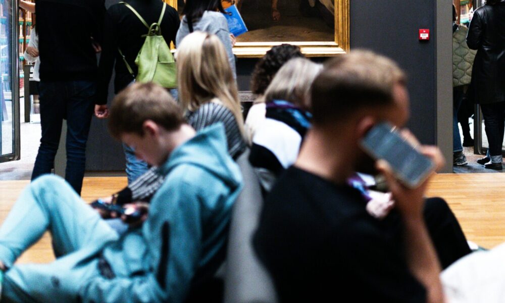 Visitors sitting and standing in a museum. People looking at art.