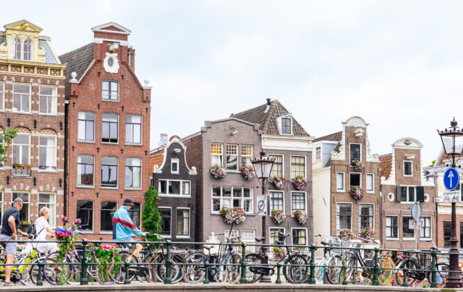 Colourful traditional Dutch houses along a canal. Many bicycles parked along the railing.