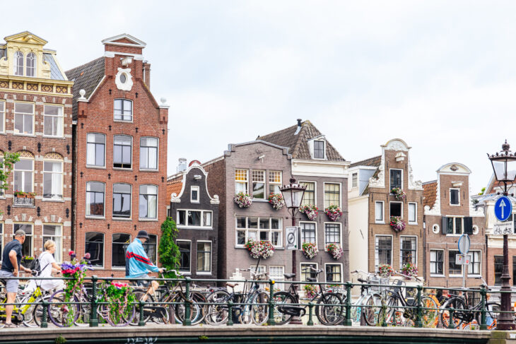 Colourful traditional Dutch houses along a canal. Many bicycles parked along the railing.