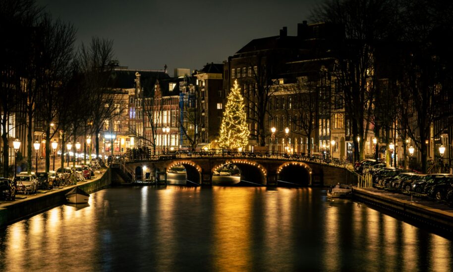 A canal in Amsterdam at night with a Christmas tree in the background. The water reflects the lights of the buildings and street lamps.