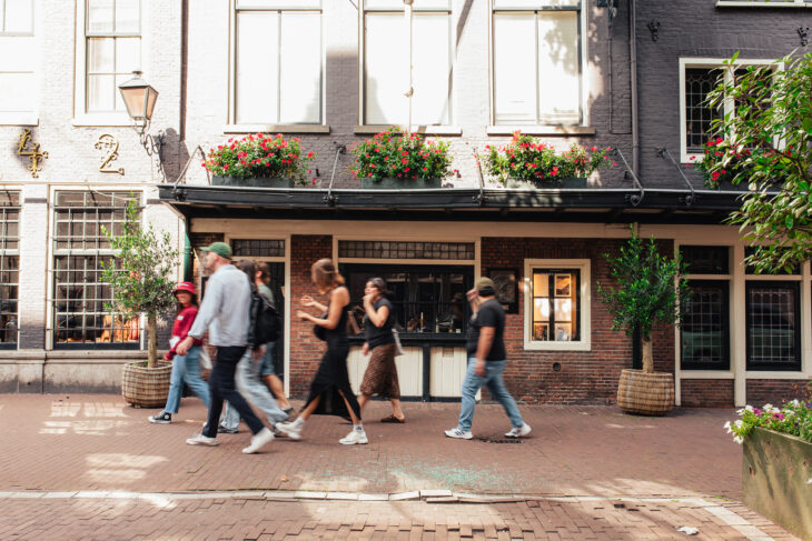 Group of people walking on a street. Colourful flowers on a building.