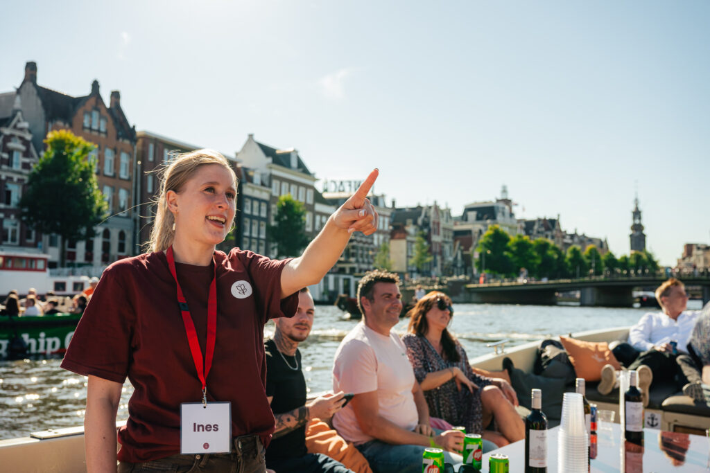 Tour guide pointing at a landmark in Amsterdam. People on a boat tour enjoying the city.